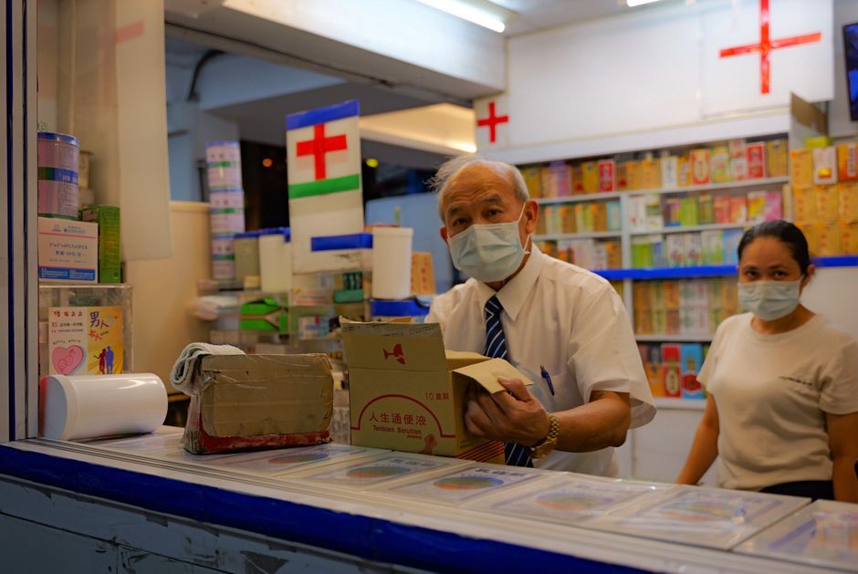 Two masked pharmacy workers organizing parcels in a Taitung pharmacy at night.